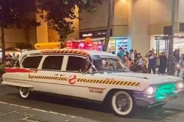 1962 Cadillac Eureka Hearse Ghostbusters Ecto-1 car with yellow-black hazard stripes on a city street at night, crowd gathered and watching.