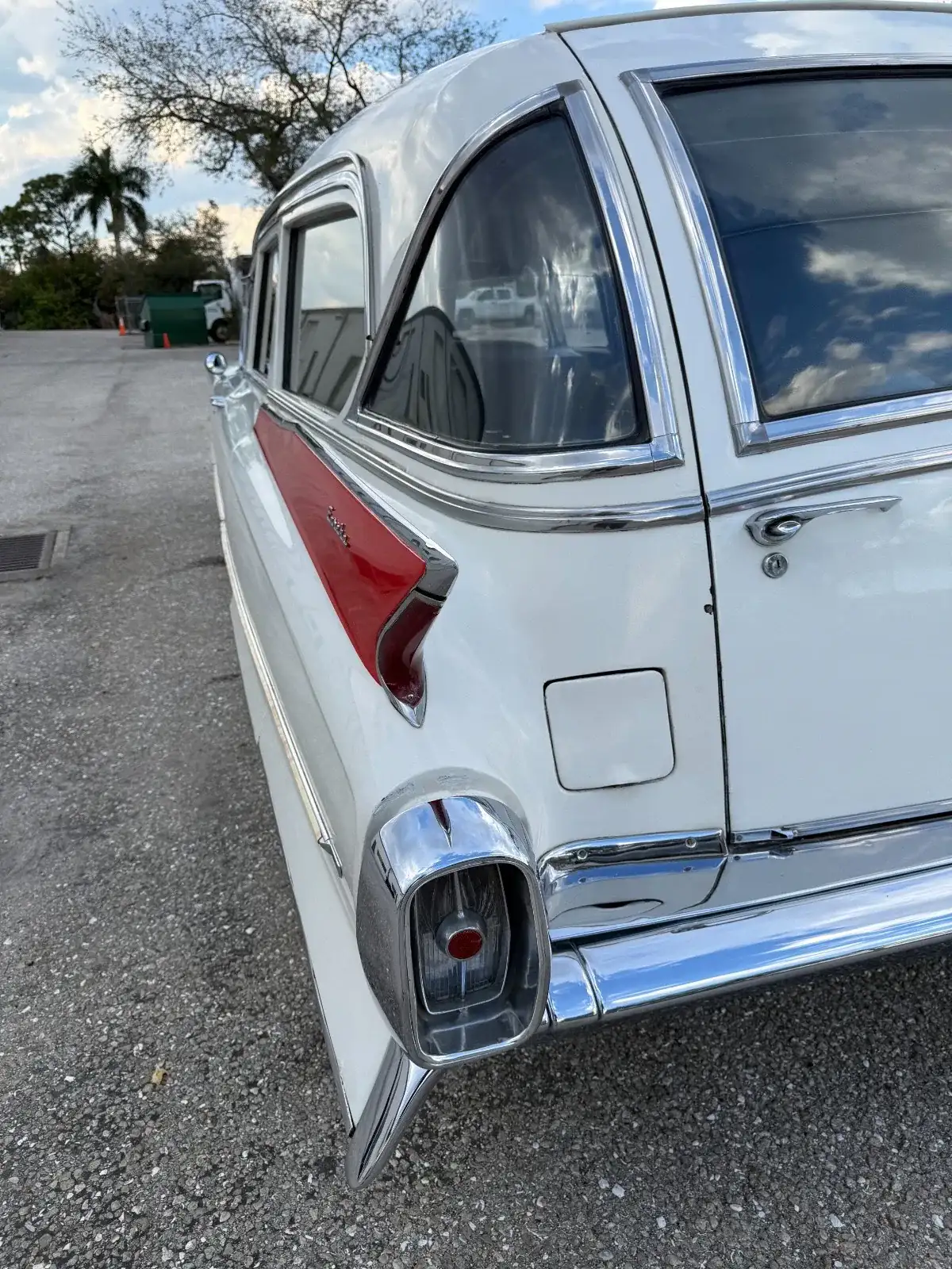 Rear quarter view of a white vintage 1962 Cadillac hearse with chrome trim and a red tail fin, parked on a paved lot.