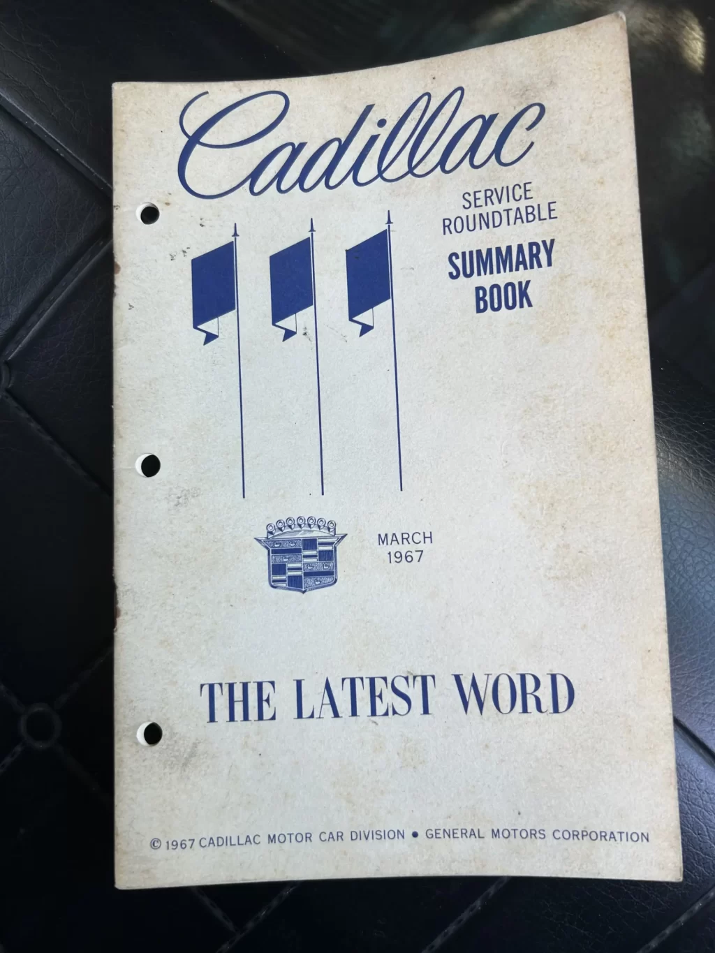 Front cover of a worn 1967 Cadillac brochure with blue graphic bars, Cadillac emblem, and 'Cadillac Motor Division' text.