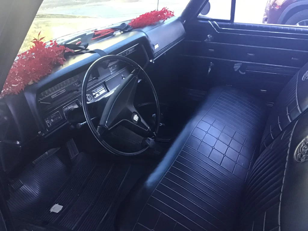 Interior of a vintage car with a black dashboard and steering wheel; red garlands draped across the dash.