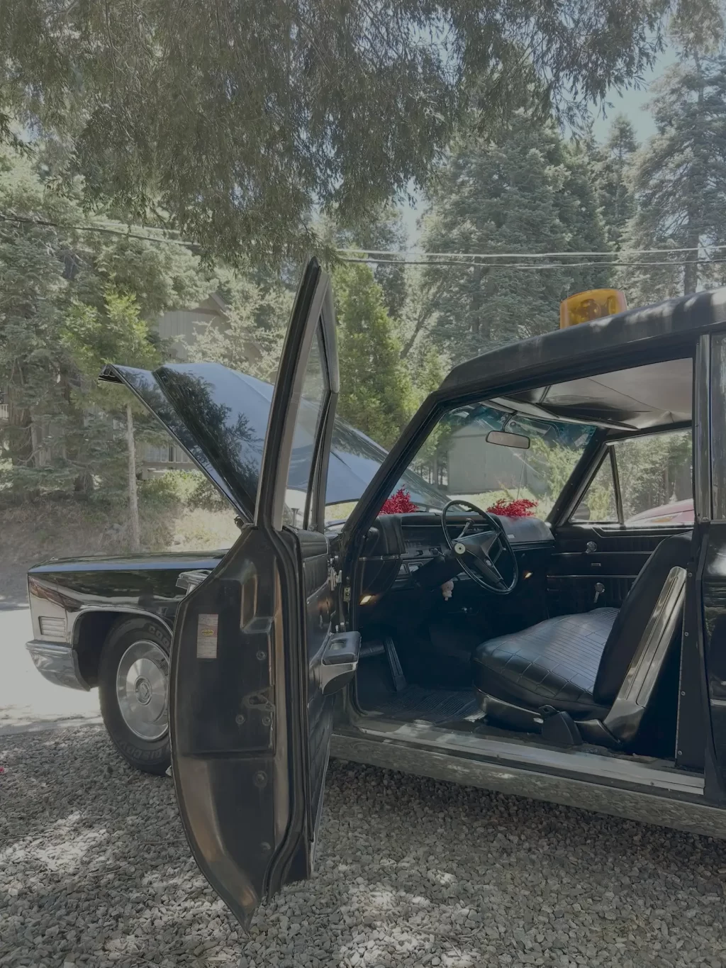 Open doors of a black vintage car on a gravel surface, exposing the interior and steering wheel with a yellow emergency light on top.