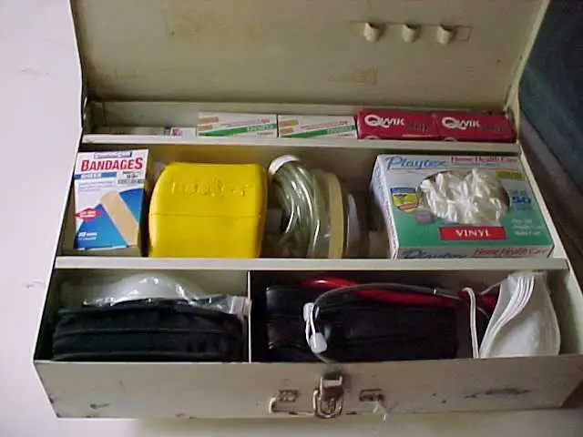 Open metal first-aid kit with a yellow labeled 'First Aid' container and compartments holding bandages, gloves, and assorted medical supplies.